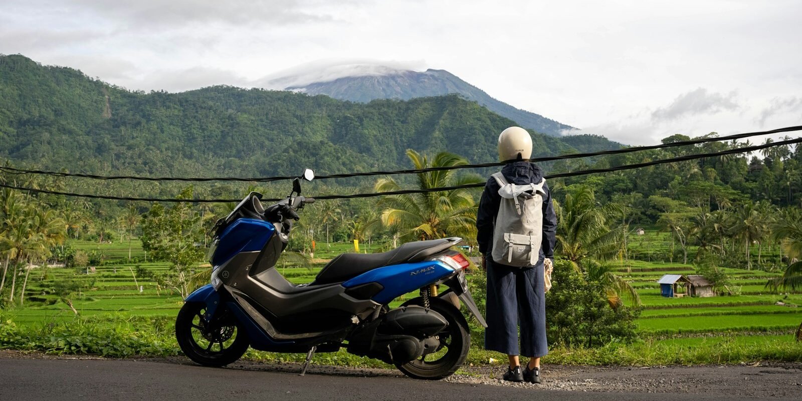 A traveller with a scooter overlooking rice fields and mountains in Bali