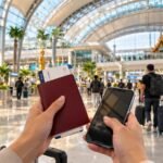 A traveller holding a passport and phone in a Thai airport arrivals hall