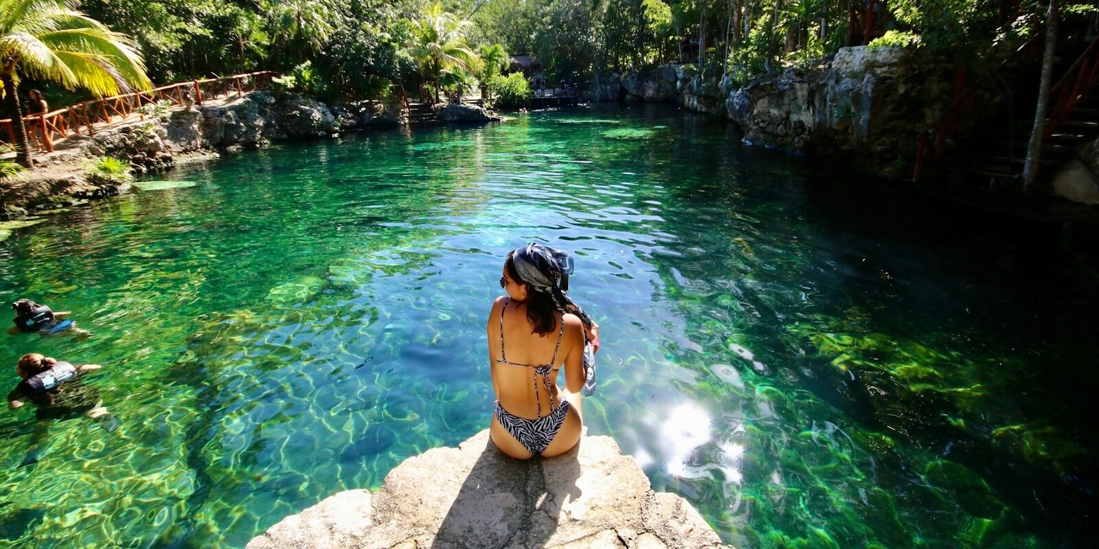 A swimmer at the edge of a turquoise cenote in the Yucatán jungle