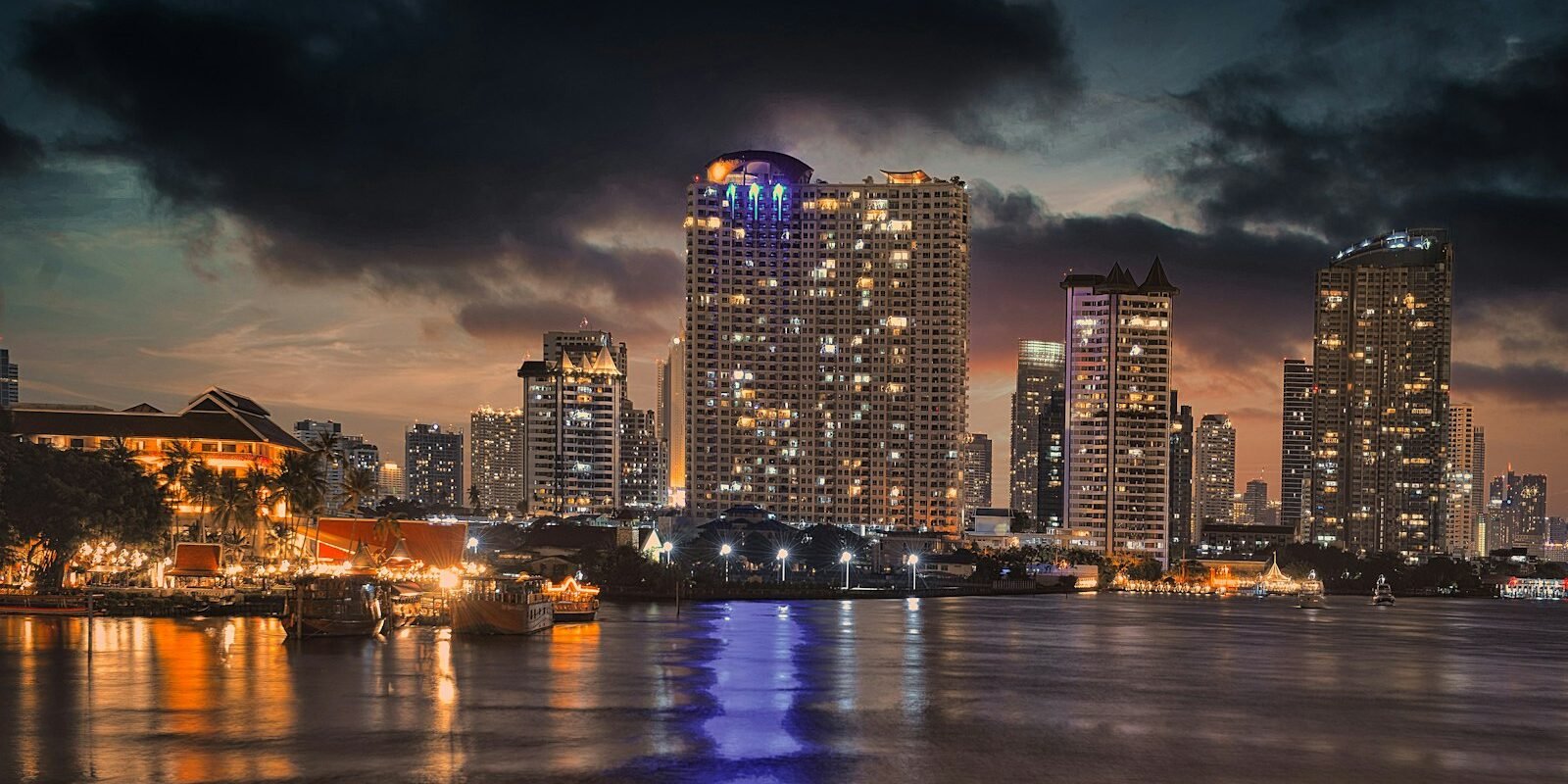 Bangkok riverside hotels and skyline lit up at night across the Chao Phraya
