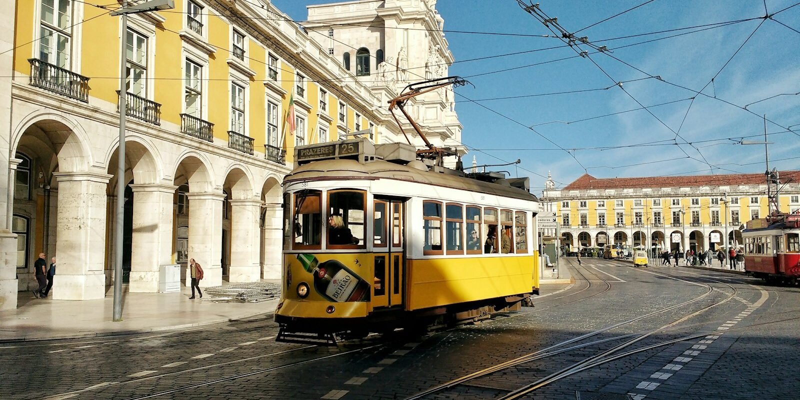 A yellow tram passing arcaded buildings in central Lisbon